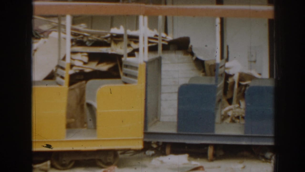 Miniature train side with blue seats, yellow panel, and damaged interior visible behind it.