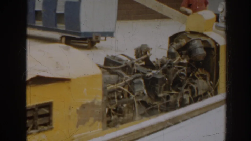 Close 8mm frame showing the damaged miniature train's yellow bodywork with exposed wires and mechanical components at the front.