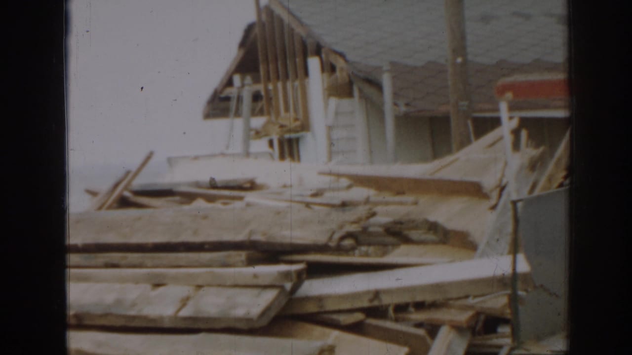 Damaged roof edge, exposed framing, and scattered boards outside a building.