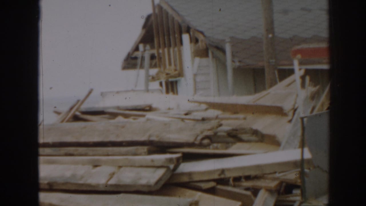Torn roof section and wooden wreckage beside a damaged structure.