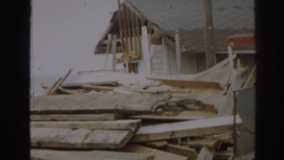 1963 New Jersey home-movie frame with exposed rafters, broken planks, and structural wreckage near a damaged building.