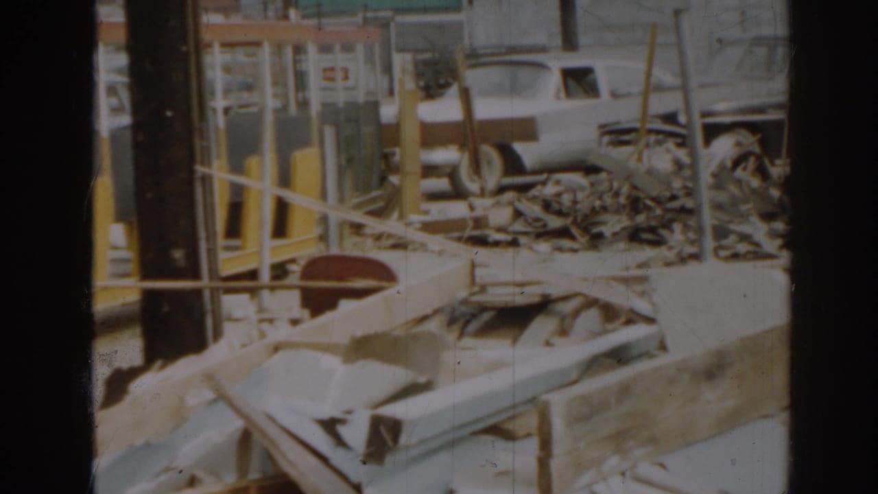 Similar view of debris and wooden rails with a white car parked beyond the site.