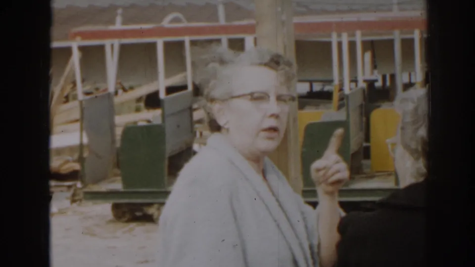 In 1963 New Jersey home-movie footage, an elderly woman in glasses points beside another adult near a large construction-site structure.
