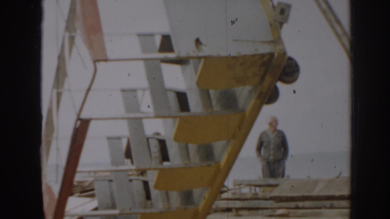 A large yellow and white metal structure dominates the frame, with a man standing nearby in the 1963 New Jersey scene.