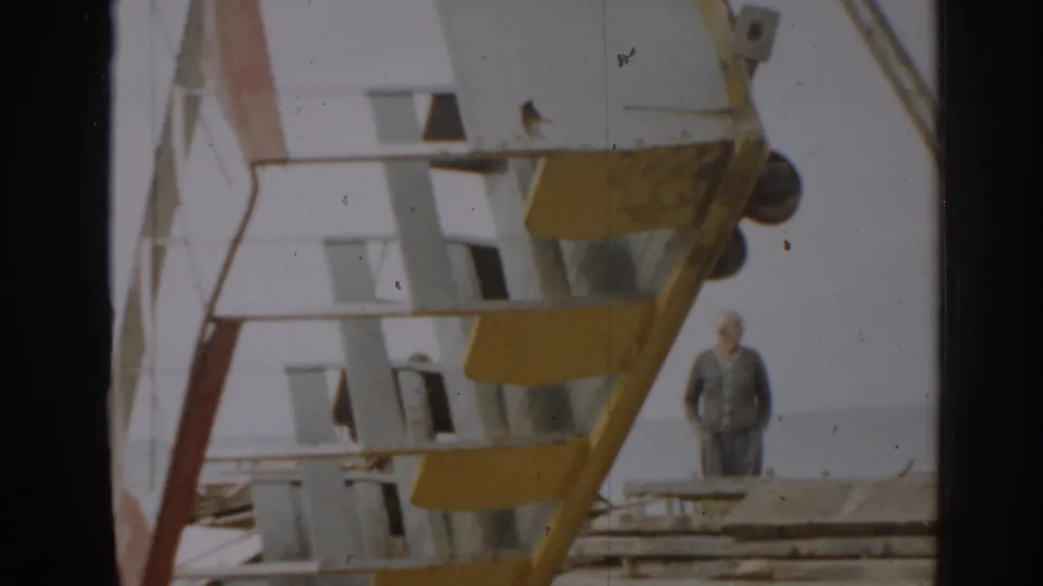 A large yellow and white metal structure dominates the frame, with a man standing nearby in the 1963 New Jersey scene.