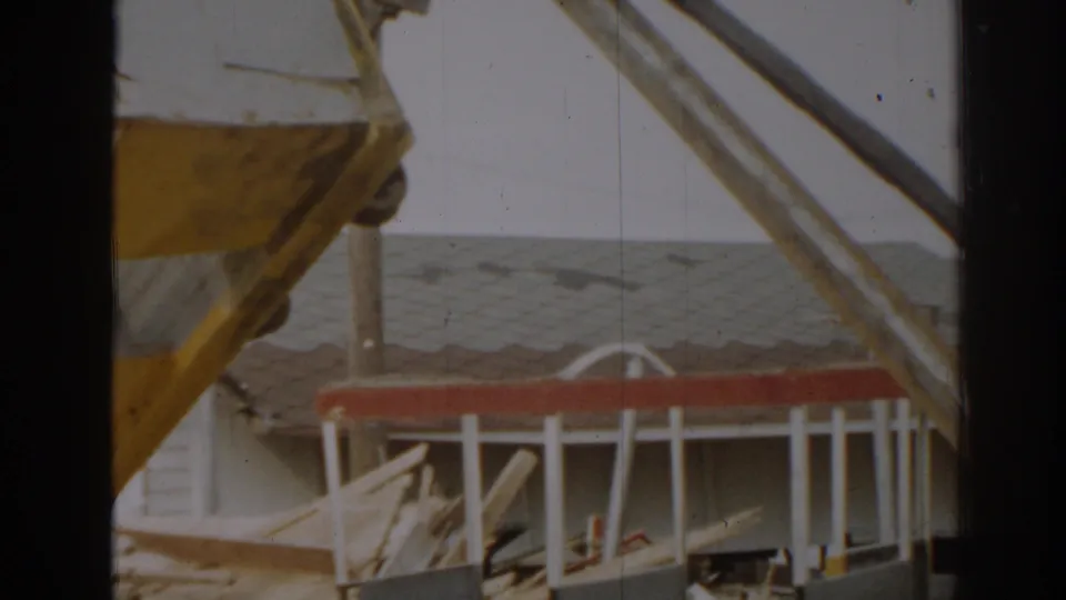 A yellow and white structure is seen over red and white framework and stacked materials in the 1963 New Jersey construction-site footage.