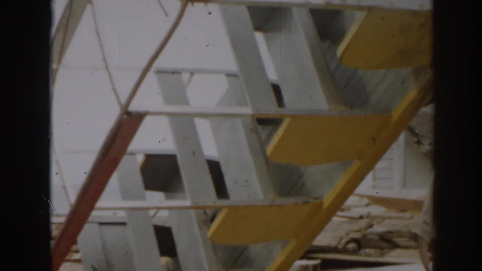 A low-angle 8mm view of painted framework, an angled red support, and scattered boards at a New Jersey damage site in 1963.