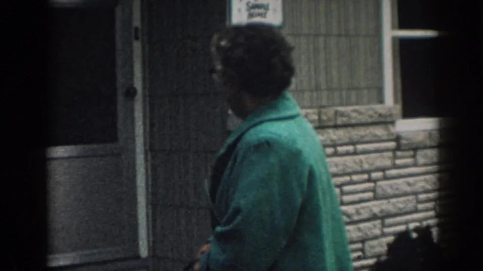 In 1963 New Jersey home-movie footage, the woman is seen from behind near the doorway and windows of the stone-faced house.