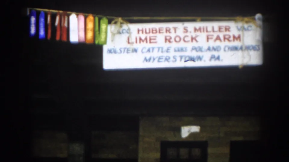 The pan ends on the Hubert S. Miller Lime Rock Farm sign and hanging livestock ribbons, with dark wooden siding behind them.