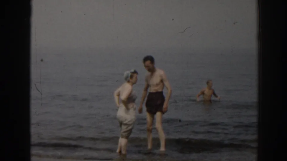 1963 New Jersey beach scene with a man and woman near the surf while another man wades farther out in the water.