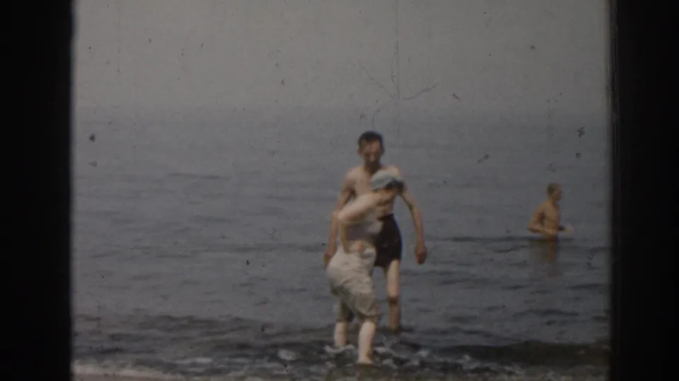 1963 New Jersey seashore footage showing two adults close together at the waterline and another adult farther out in the calm surf.