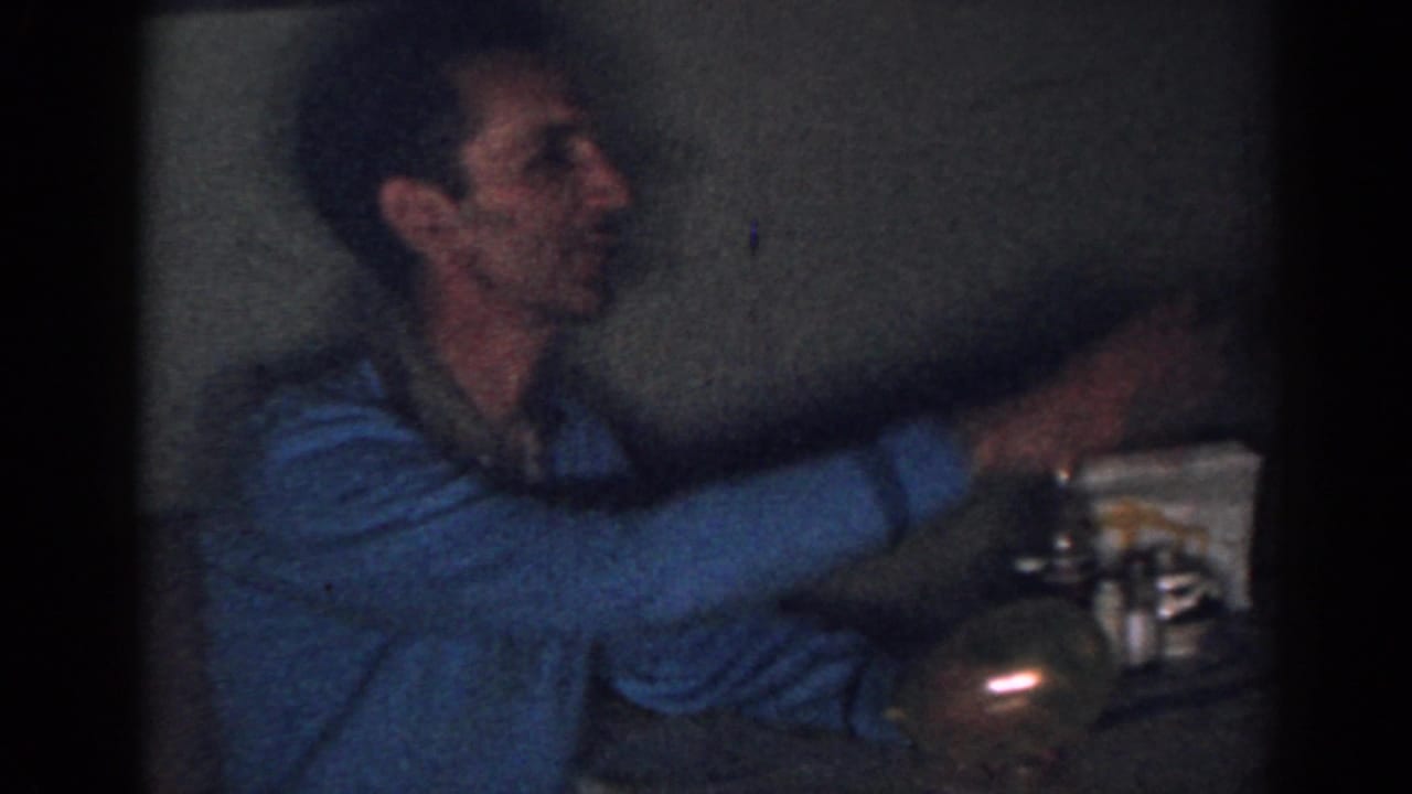 Man in a blue sweater reaches toward items on a small table.