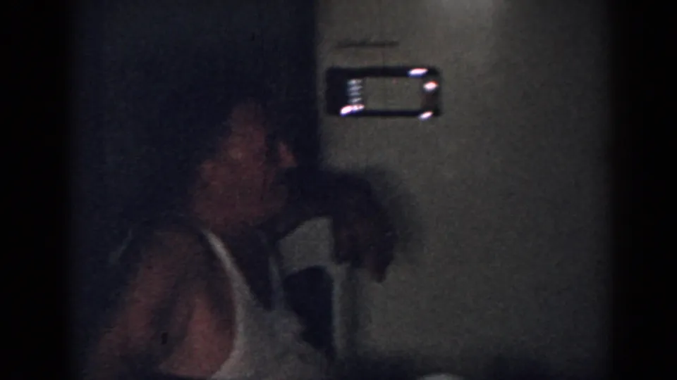1963 New Jersey home-movie frame showing a dim kitchen with a man in glasses beside a woman wearing a light apron.