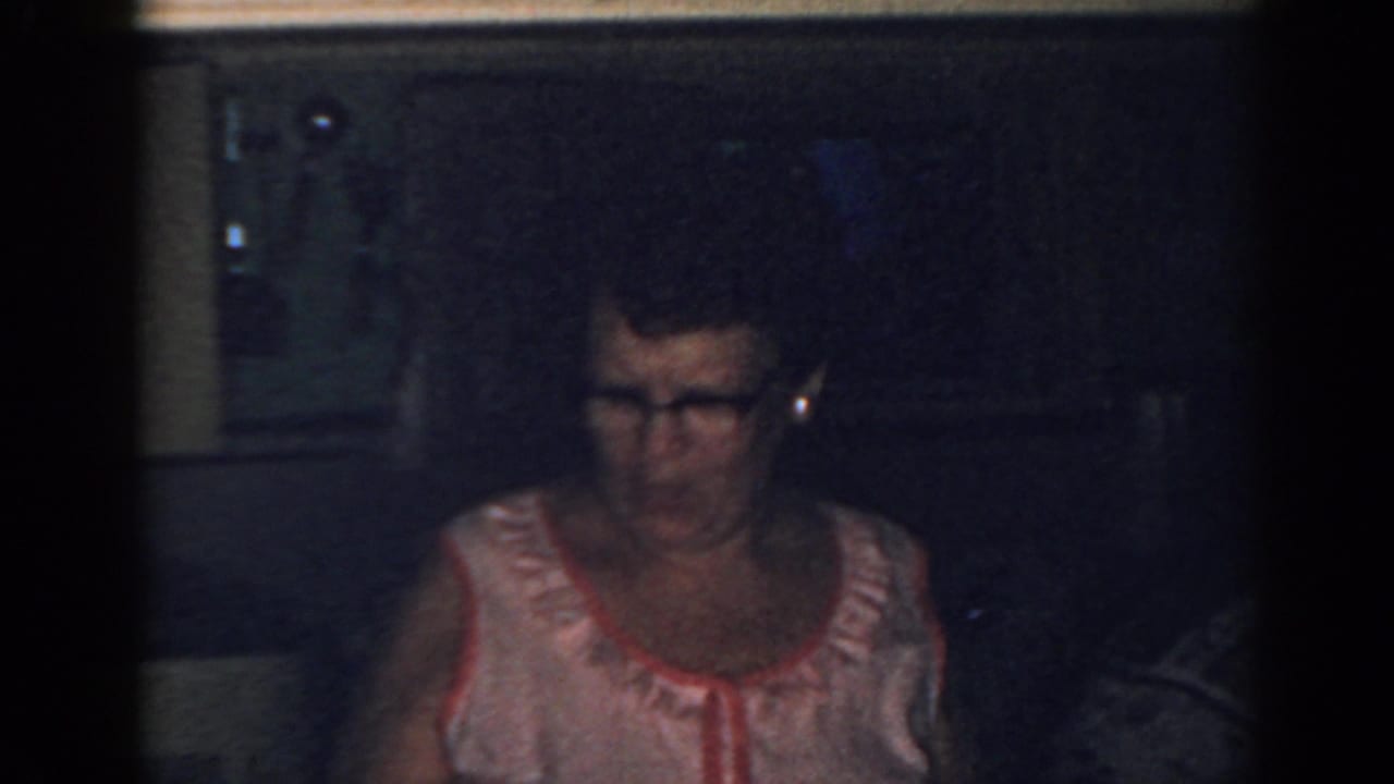 Adult woman with glasses looks downward in a dark kitchen.