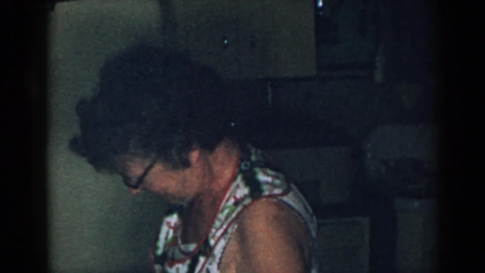 Older woman wearing glasses looks down while working at a counter in a 1963 New Jersey kitchen interior.
