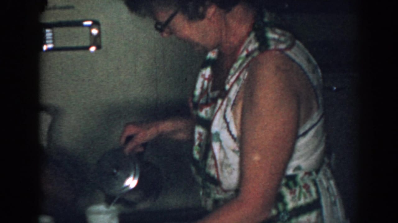 Woman in glasses pours coffee beside a kitchen table in a dim interior.
