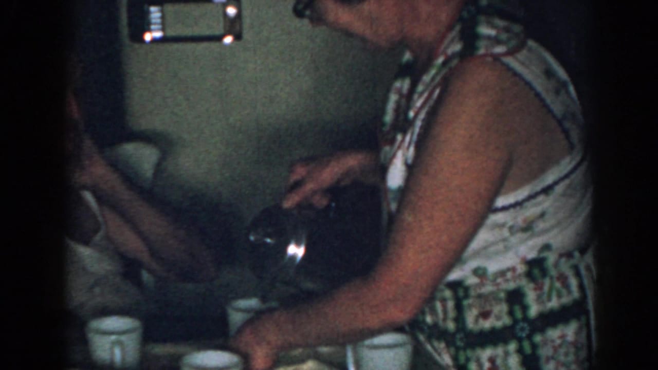 Woman pours coffee from a glass pot while mugs sit on the table.