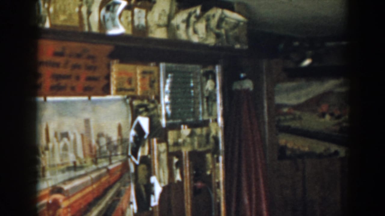 Dim room wall with framed items, shelves, a red curtain, and a painted train scene partly visible.