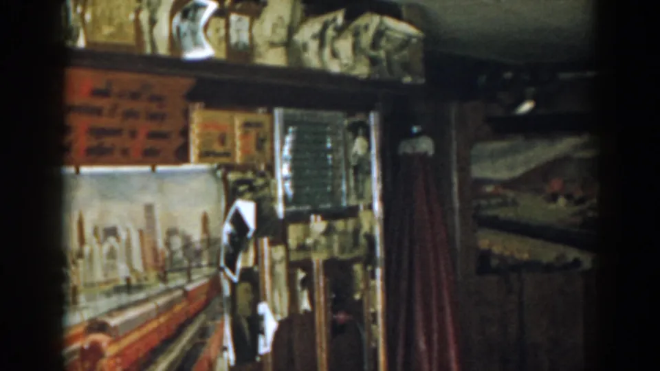 1963 New Jersey 8mm frame showing a dim private room with shelves, wall displays, a red curtain, and railroad-themed decoration.