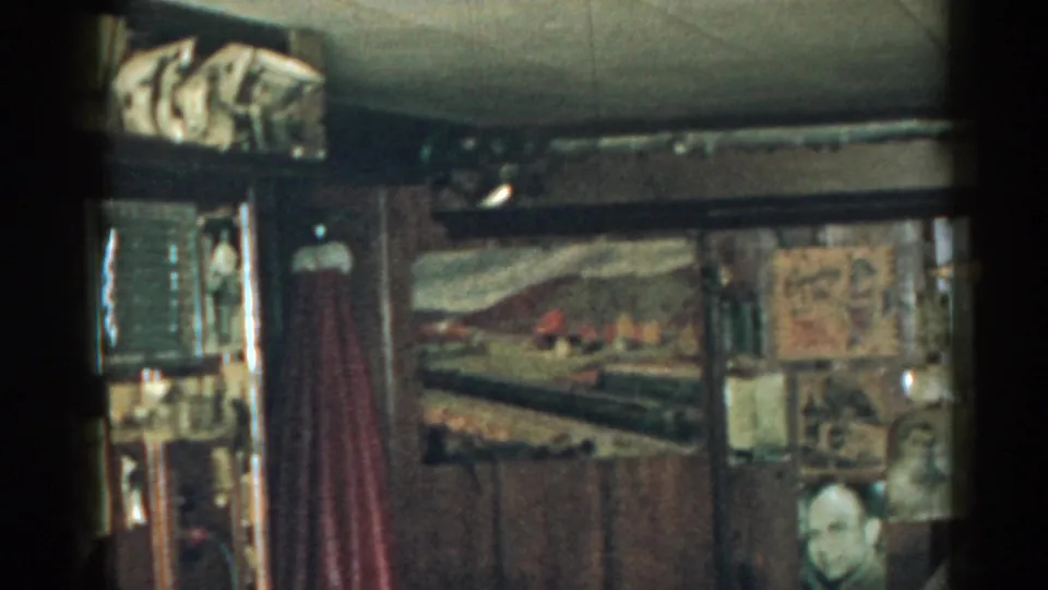 1963 New Jersey 8mm frame showing a private room wall with railroad art, memorabilia, red curtain, and a partial face or bust near the lower edge.