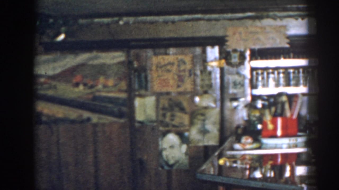 Bar counter and shelves with glassware, red containers, framed pictures, and a visible face image.