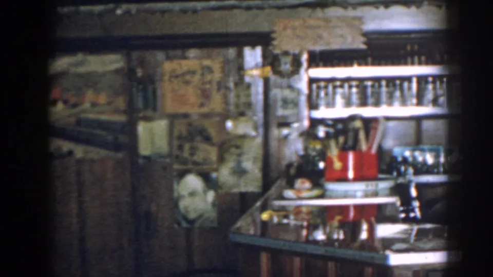 1963 New Jersey 8mm frame showing stored glasses on bar shelving with framed art, wood paneling, and counter items.