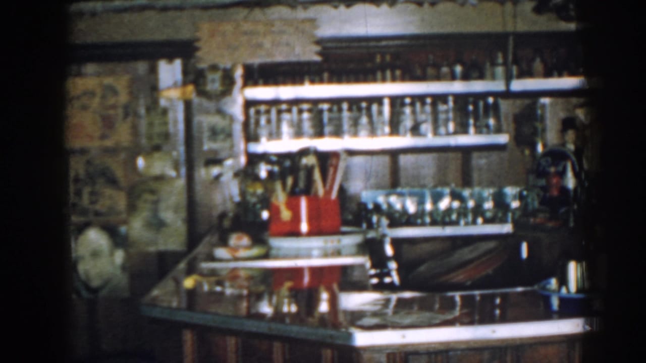 Bar shelves and counter with bottles, glasses, and a blue tray at right.