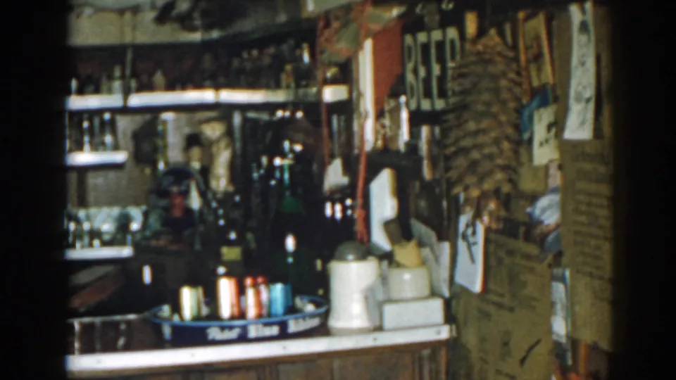 1963 New Jersey interior frame with a BEER sign, bottle shelves, ceramic jugs, colorful cans, and a crowded right-side wall display.