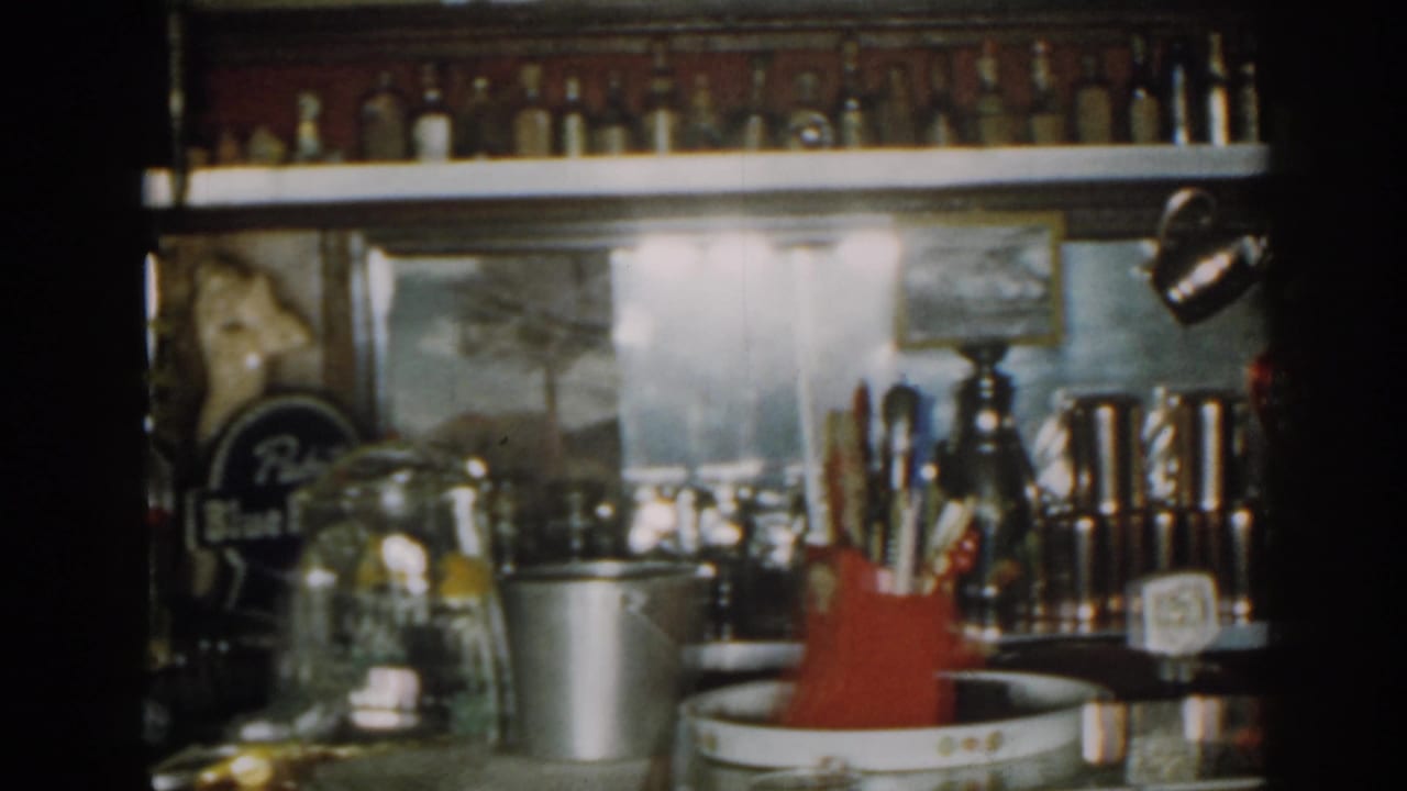 Bar display with bottles, glasses, metal pails, red utensil holder, and drink tools.