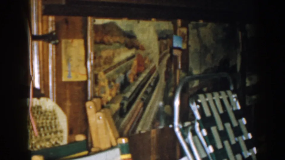 1963 New Jersey home-movie frame centered on a painted train mural with chairs and household storage nearby.