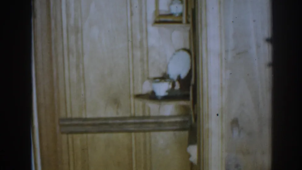 1963 New Jersey 8mm frame showing a paneled corner, a small recessed shelf, and white ceramic dishes inside a private home.