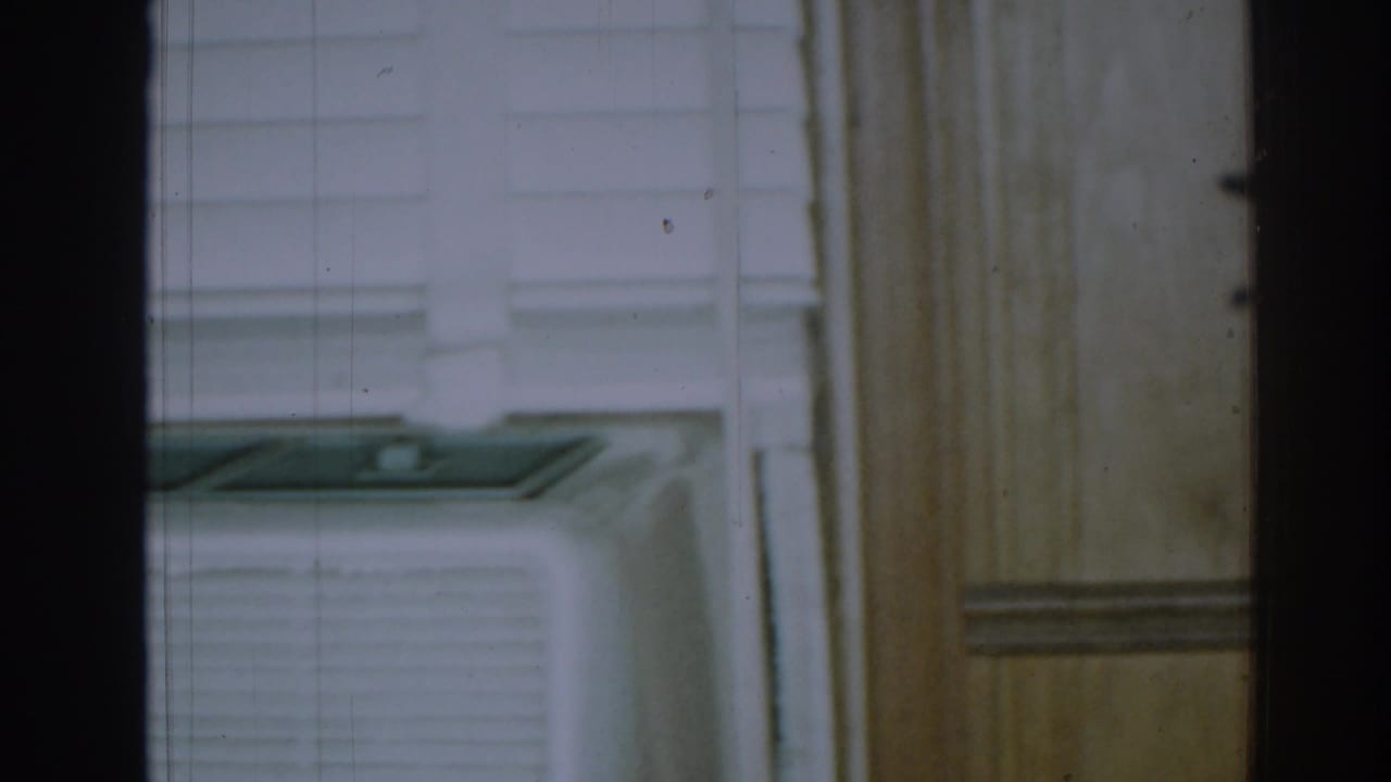 Window air conditioner seen through dark vertical framing and interior trim.