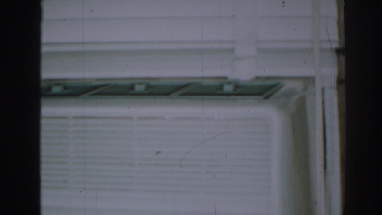 Close view of a window air conditioner and blinds behind dark framing.