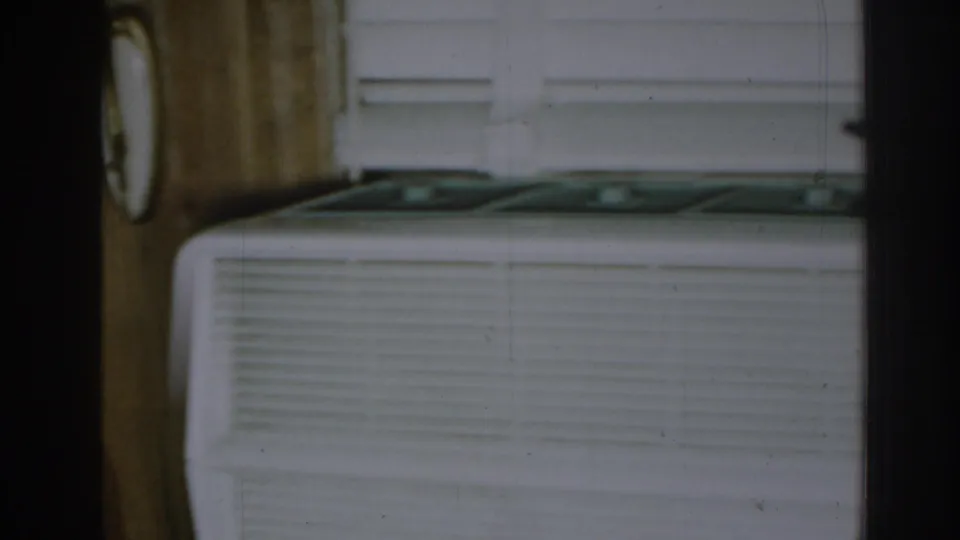 Interior frame showing a white window air conditioner beneath blinds, bordered by wood trim and dark vertical framing.