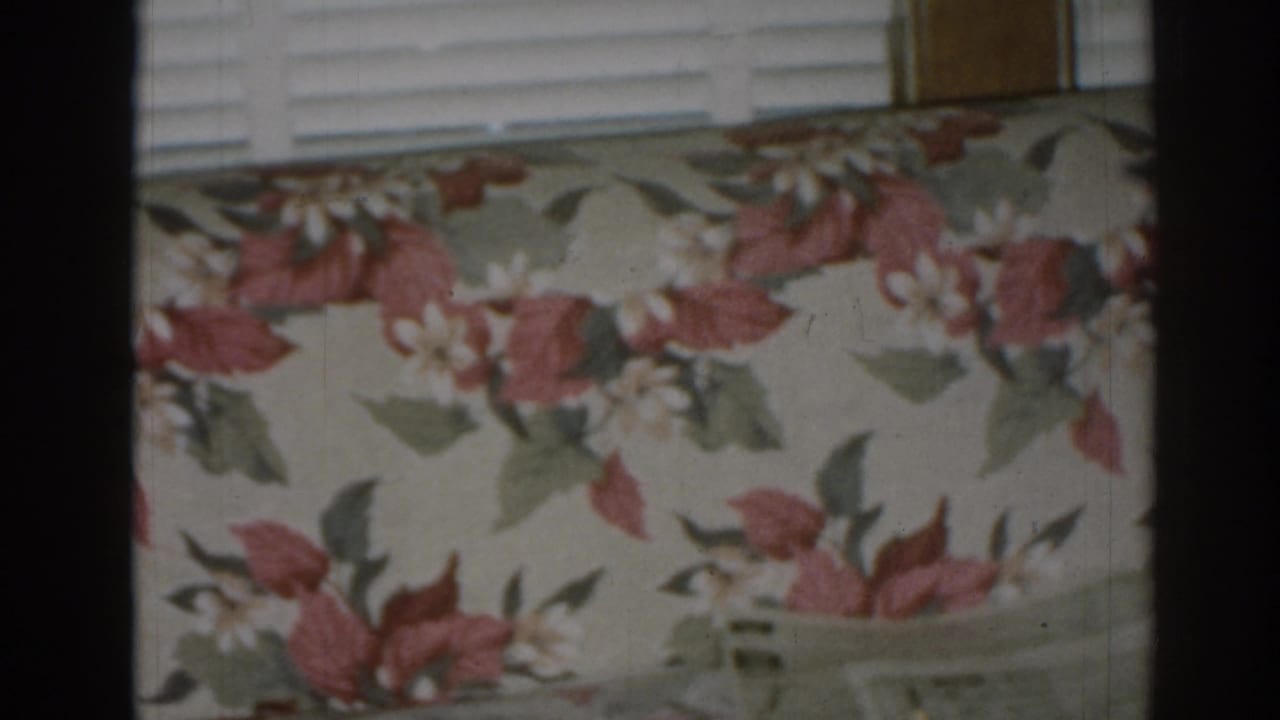 1963 New Jersey home interior detail of a floral sofa back set against white blinds and warm wood window trim.