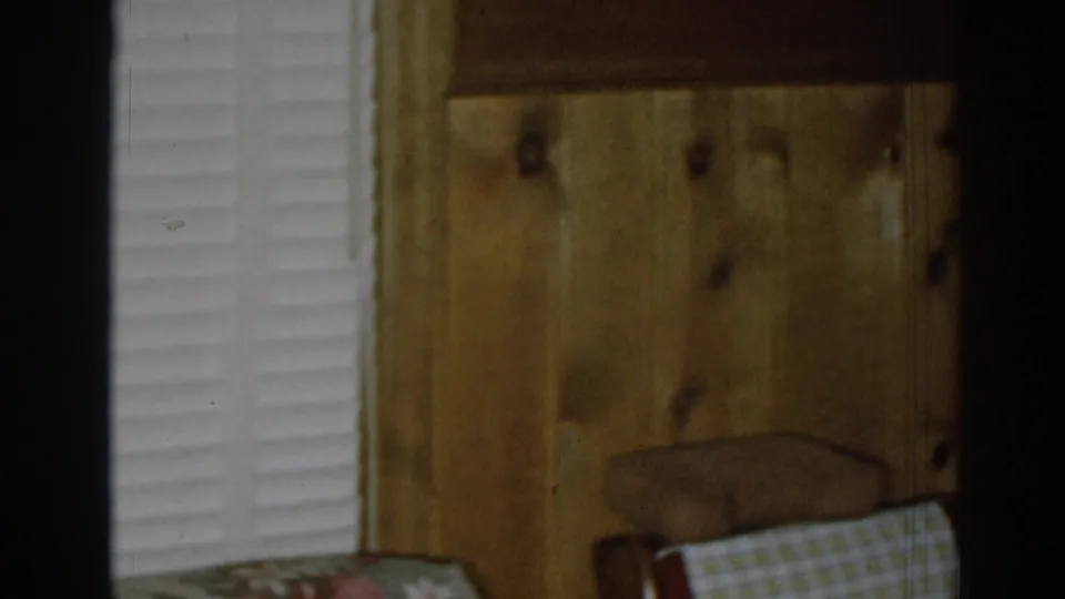 1963 New Jersey home-movie frame showing wood paneling, a shuttered window, an upholstered chair, and a wall-mounted lamp.