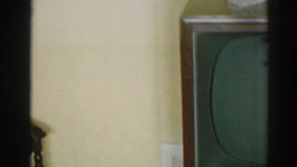 1963 New Jersey interior frame showing a console television below a pale wall, with wood paneling and chair details above.