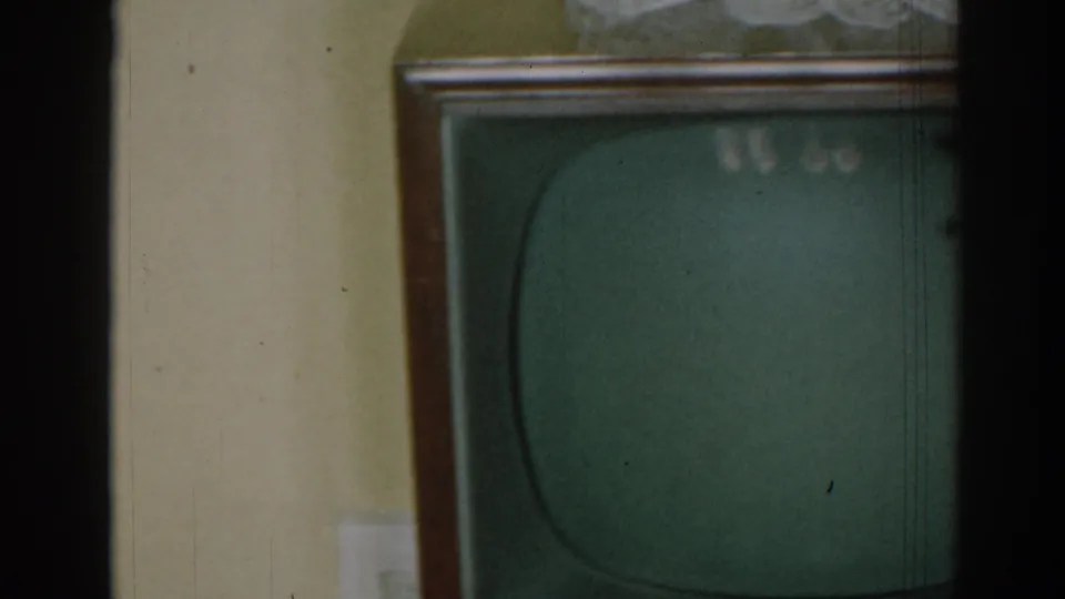 1963 New Jersey home interior with a dark-screen console television, pale wall, wood paneling, and a partial armchair.