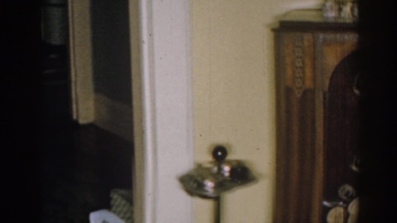 Dim interior corner with dark wood cabinet, metal ashtray stand, pale wall, and doorway trim.