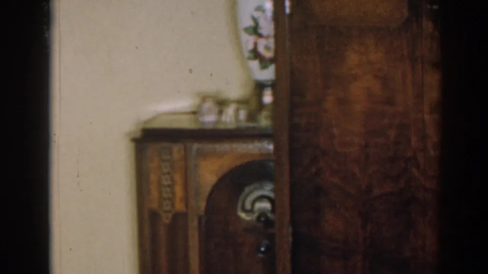 1963 New Jersey interior detail with a floral vase and small cups on a dark wood cabinet against a pale wall.