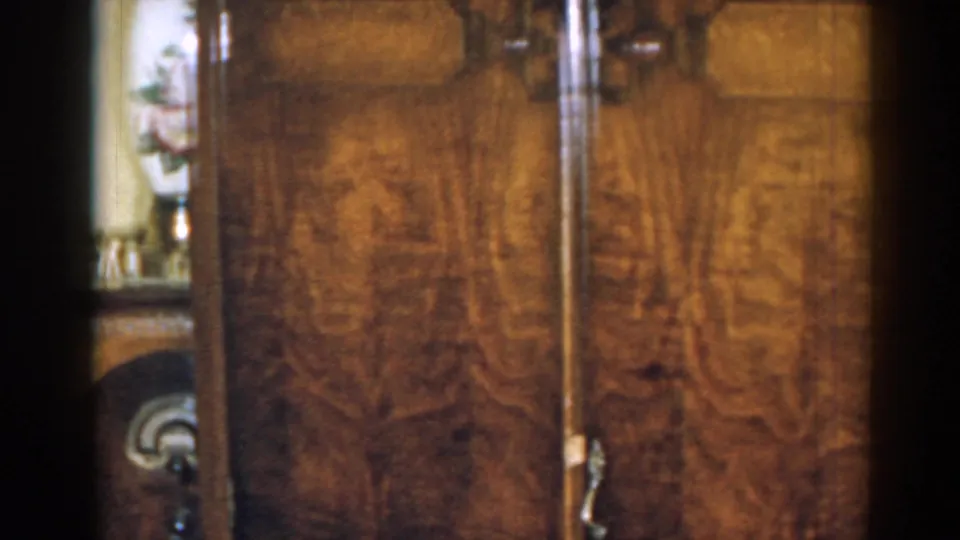 Close, soft 8mm view of wood furniture in a 1963 New Jersey home interior, with vase and figurines at the edge.