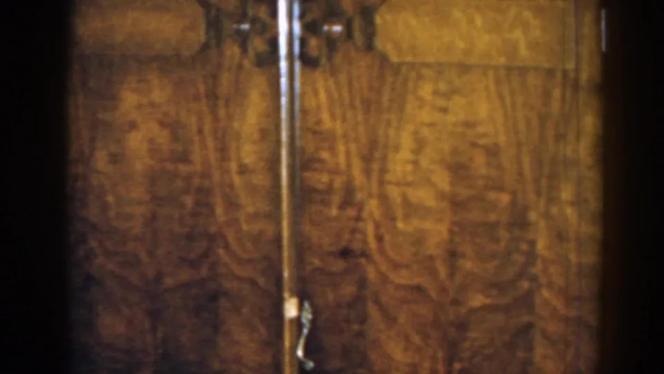 Close 1963 New Jersey home-movie frame of a large wooden cabinet, showing warm wood grain and a metal handle.