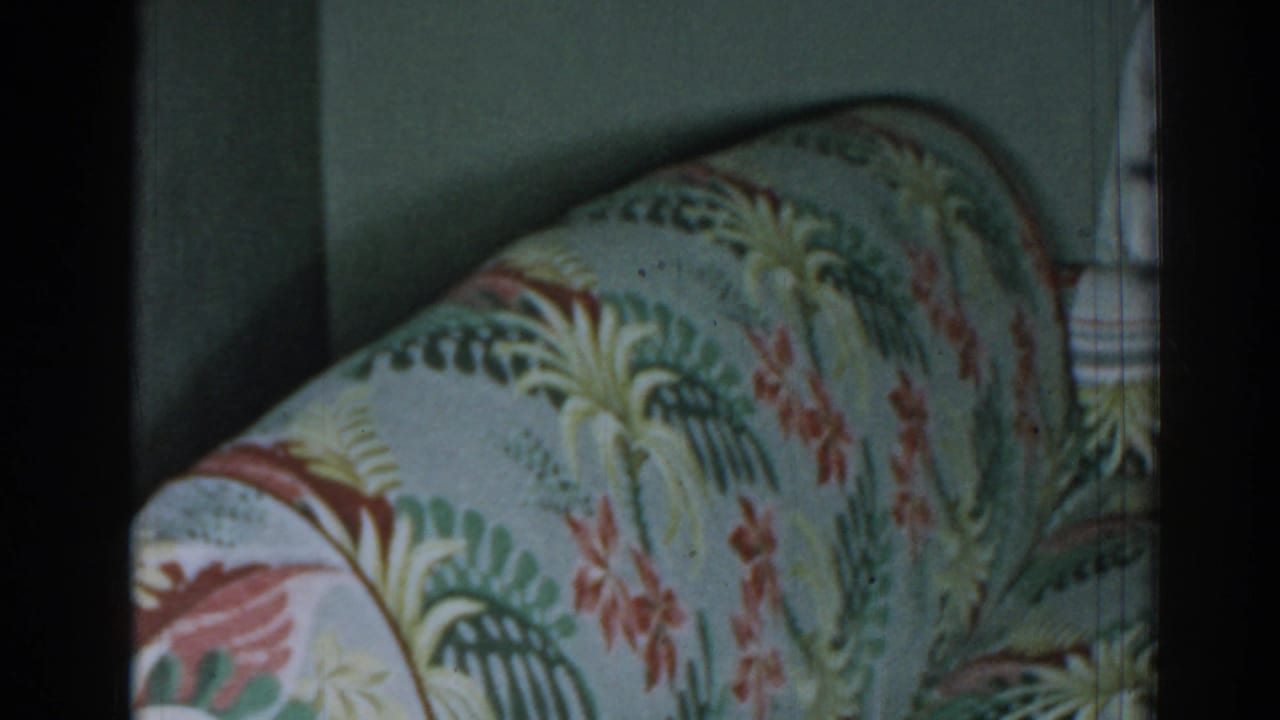 Curved patterned sofa arm beside a muted green wall and floral curtain.