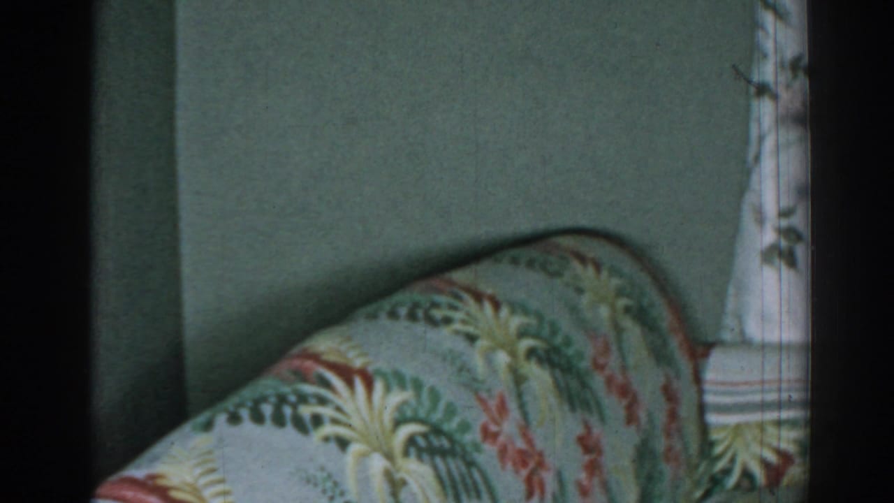Patterned sofa back and arm next to a floral curtain and green wall.