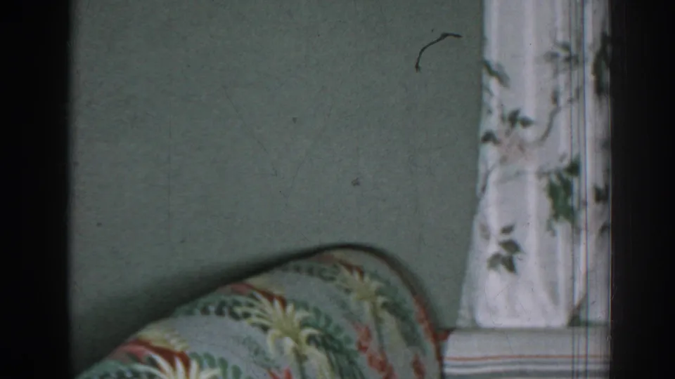1963 New Jersey home interior showing the sofa arm lower in frame with floral curtain, wall, and visible film dust.