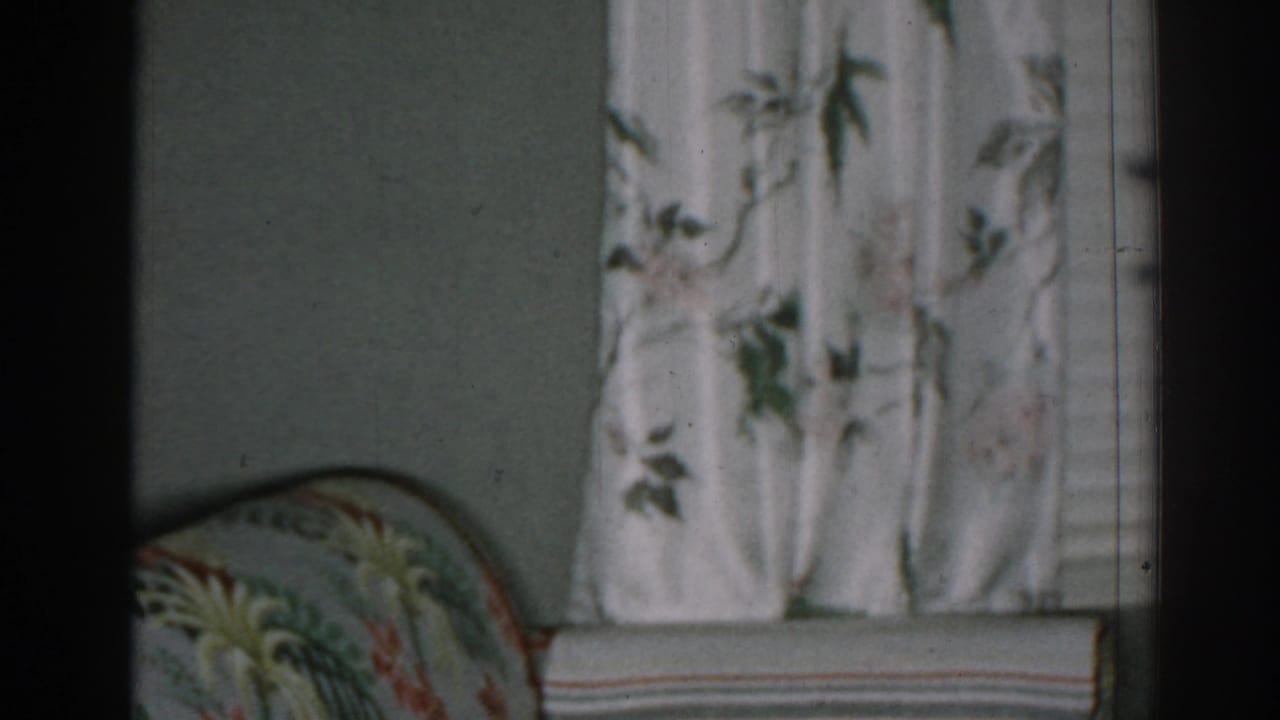 Floral curtains beside a patterned armchair in a dim living room.