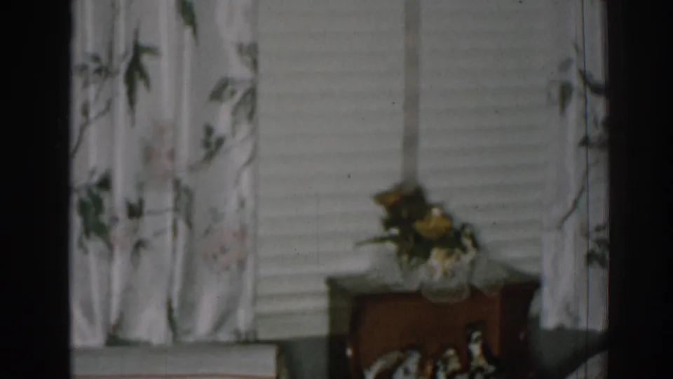 1963 New Jersey home interior showing a wooden side table, flower vase, horizontal blinds, and floral curtains.