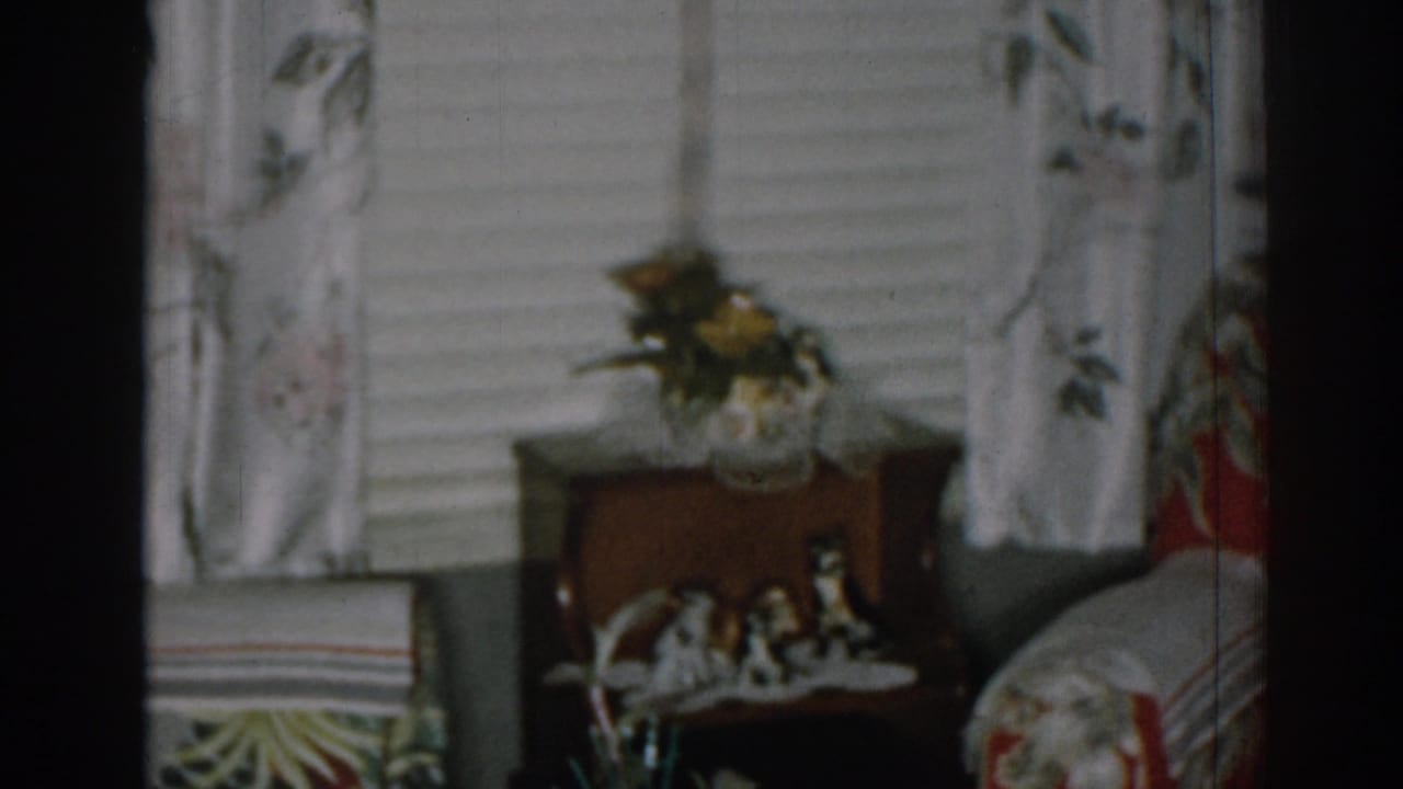 Red floral armchair beside a window and wooden side table with figurines.
