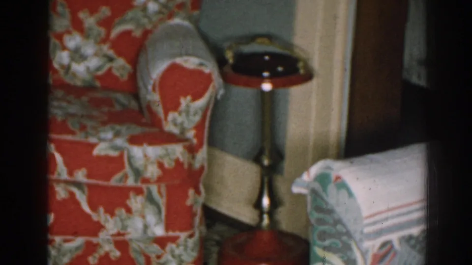 1963 New Jersey home interior with the red floral chair, brass-toned side table, and a partial pale patterned sofa entering the frame.
