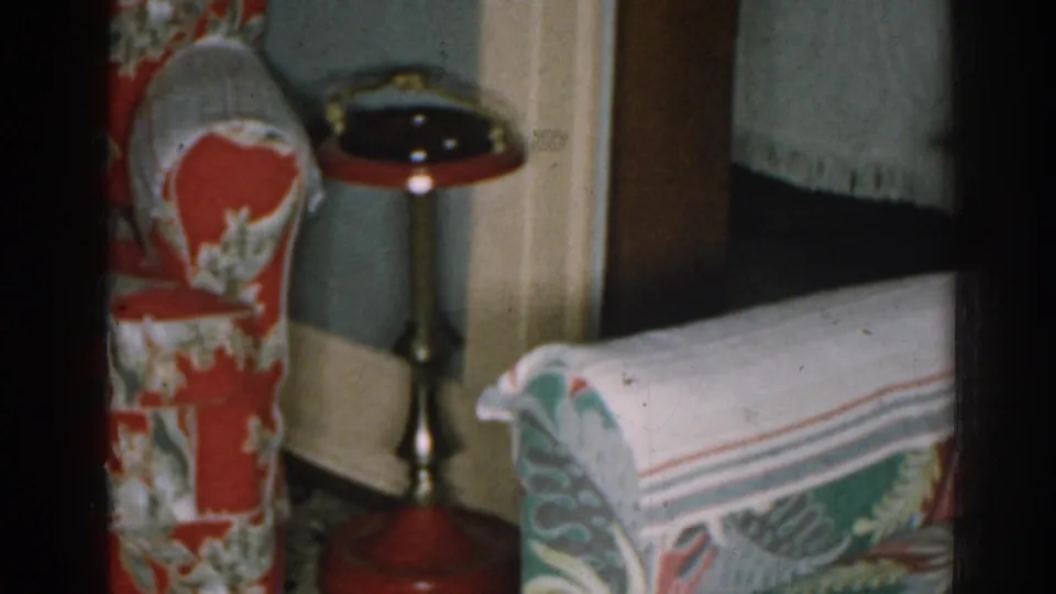 1963 New Jersey living room frame showing the floral armchair, side table, doorway edge, and partial pale sofa during a slow pan.